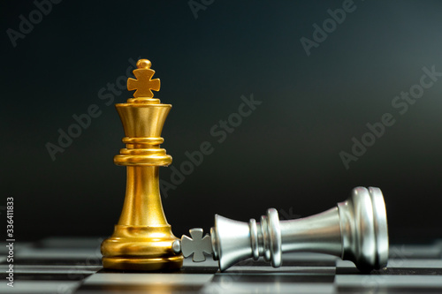 Gold king chess piece win over lying down silver king on black background