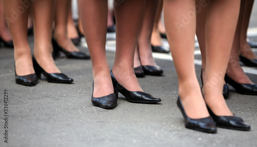 Women's legs in identical black shoes stand in formation. © Vital
