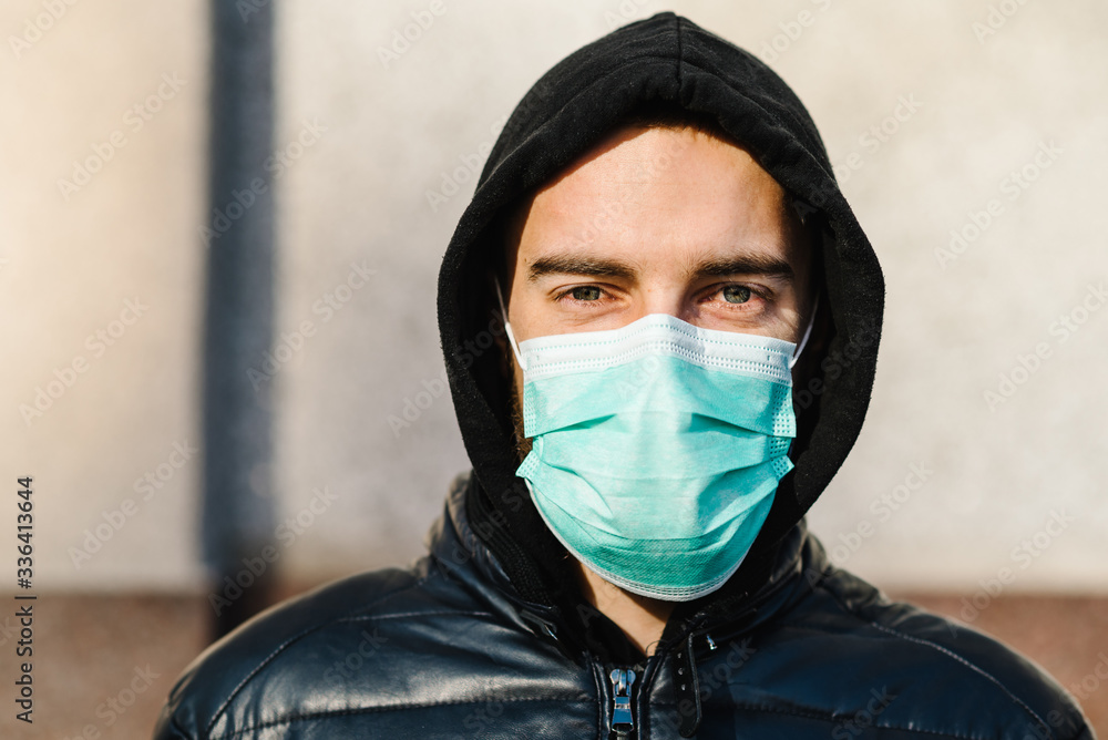 COVID-19 Pandemic coronavirus. Young man in city street wearing face mask protective for spreading of disease Covid-19. Close up of man with surgical mask on face against SARS-CoV-2. COVID-19 Pandemic coronavirus. Young man in city street wearing face mask protective for spreading of disease Covid-19. Close up of man with surgical mask on face against SARS-CoV-2.