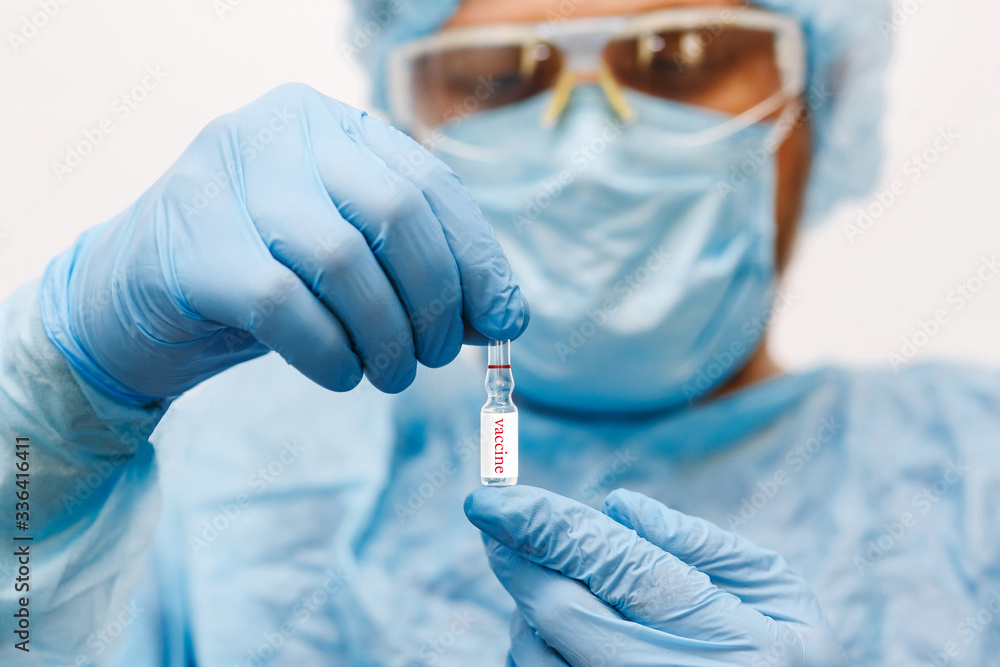Close up of doctor hand holding vaccine. Medical equipment. A doctor wearing personal protective equipment including mask, goggle, and suit to protect COVID coronavirus infection. Close up of doctor hand holding vaccine. Medical equipment. A doctor wearing personal protective equipment including mask, goggle, and suit to protect COVID coronavirus infection.