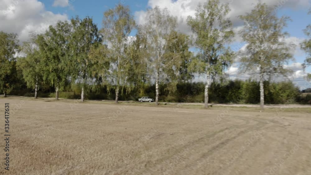 Aerial view of white soviet retro car driving on dirt road through tree alley Aerial view of white soviet retro car driving on dirt road through tree alley