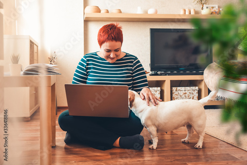 Woman works online using laptop computer, dog interferes. Quarantine coronavirus photo