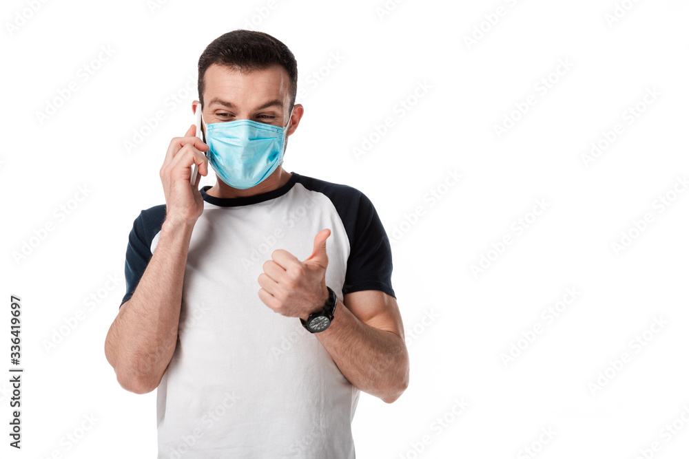 man in medical mask talking on smartphone and showing thumb up isolated on white man in medical mask talking on smartphone and showing thumb up isolated on white