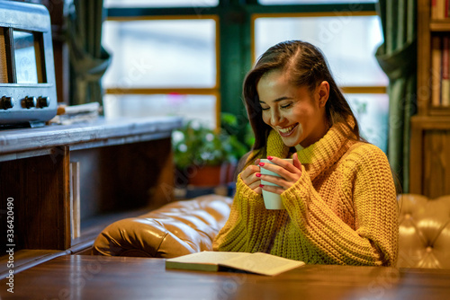 The beautiful woman reading a book on the sofa in front of the window with a cup of coffee