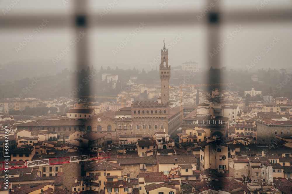 Palazzo Vecchio and the centre of Florence seen through the metal fence from the dome of Florence Cathedral on a foggy day
