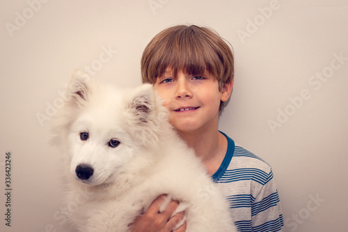 Cute boy holding his puppy samoyed dog posing for camera.