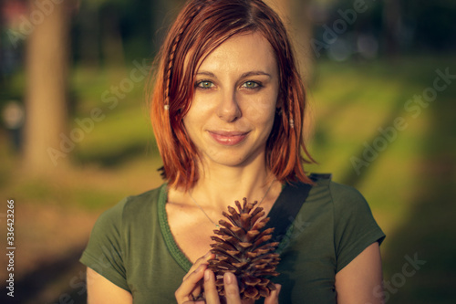 Redhead model posing and holding a pine cone