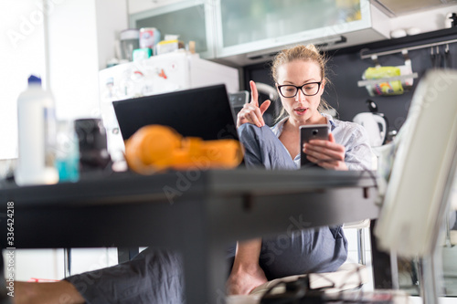 Stay at home and social distancing. Woman in her casual home clothing working remotly from kitchen dining table. Video chatting using social media with friend, family, business clients or partners photo