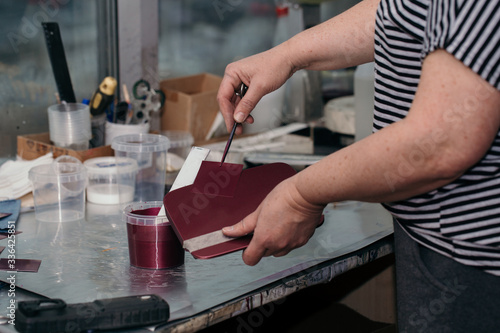 The painter’s hands hold a test plate with a paint applied on it, matched to the color of the car’s hatch and the burgundy car part