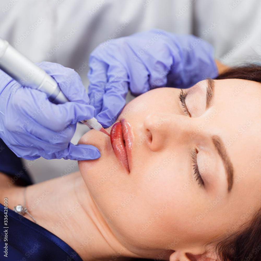 Young woman having permanent makeup on lips in beautician salon. Close up