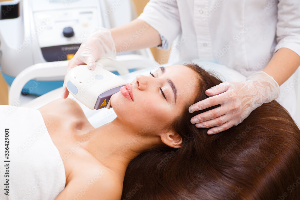 The procedure of photoepilation in the beauty salon. A young woman is removed unwanted hair on her face. Hardware cosmetology. Close up The procedure of photoepilation in the beauty salon. A young woman is removed unwanted hair on her face. Hardware cosmetology. Close up