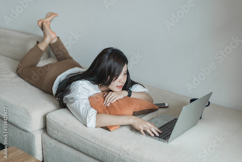 Happy young asian woman with a laptop relaxed on the sofa at home.