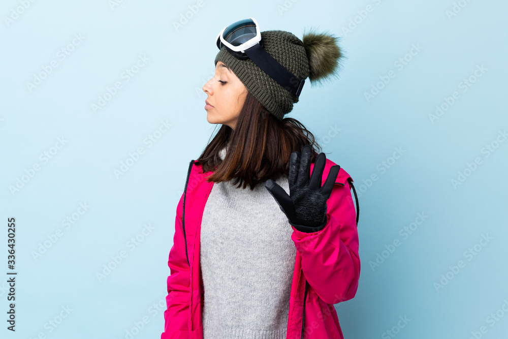 Mixed race skier girl with snowboarding glasses over isolated blue background making stop gesture and disappointed. Mixed race skier girl with snowboarding glasses over isolated blue background making stop gesture and disappointed.