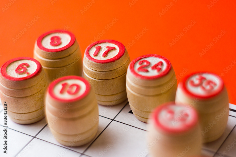 Lotto wooden barrels with numbers on a bright orange background. Some details are out of focus. Family bingo game. Conceptual photo. Lotto wooden barrels with numbers on a bright orange background. Some details are out of focus. Family bingo game. Conceptual photo.
