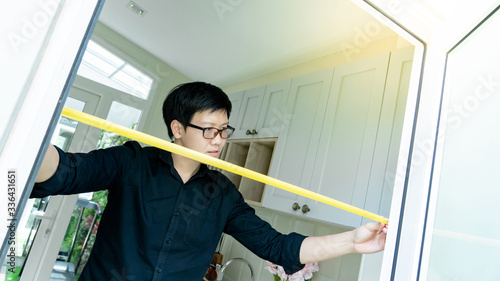 Young Asian worker man using tape measure on door frame in the kitchen. Home interior designer measuring elements on site. Housing design and construction concept