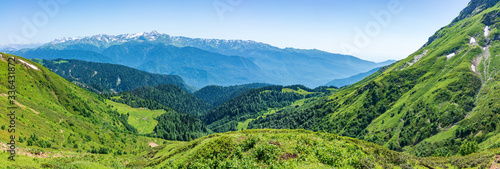 Panoramic view over the Green Valley, surrounded by high mountains with snow on a clear summer day.