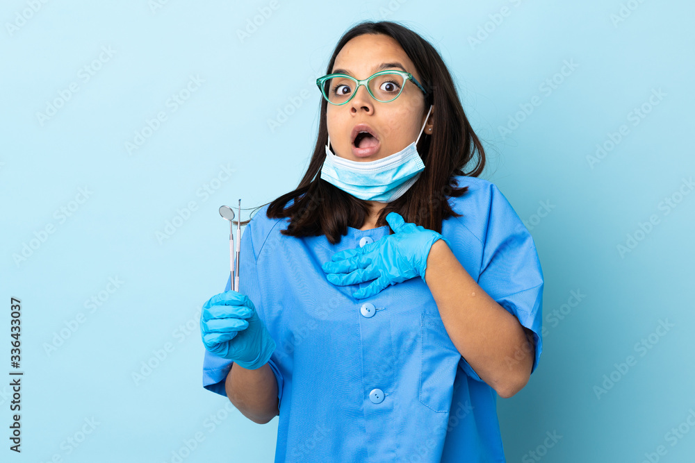 Young brunette mixed race dentist woman holding tools over isolated background doing surprise gesture while looking to the side Young brunette mixed race dentist woman holding tools over isolated background doing surprise gesture while looking to the side