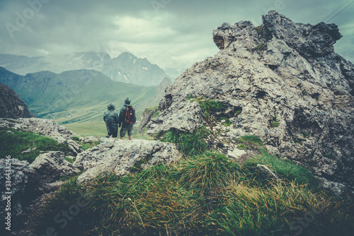 two hikers observe the valley from the top of a mountain on a cloudy day