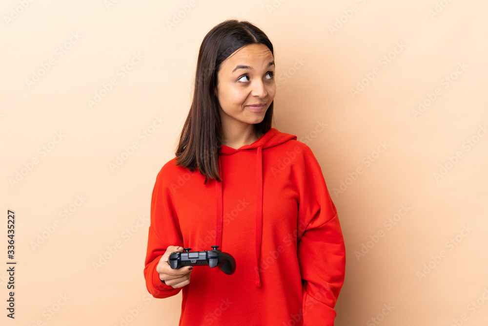 Young brunette mixed race woman playing with a video game controller over isolated background standing and looking to the side Young brunette mixed race woman playing with a video game controller over isolated background standing and looking to the side