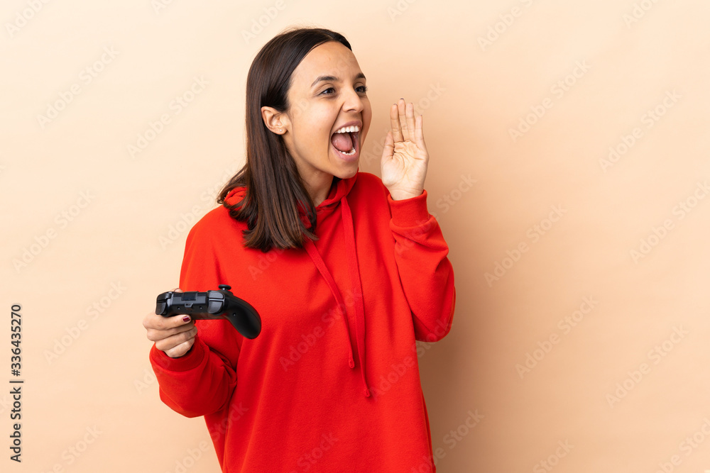 Young brunette mixed race woman playing with a video game controller over isolated background shouting with mouth wide open Young brunette mixed race woman playing with a video game controller over isolated background shouting with mouth wide open