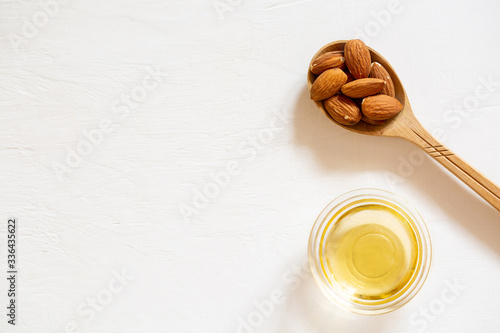 Nut almonds in a wooden spoon on a white background. Natural almond seed oil in a glass bowl.