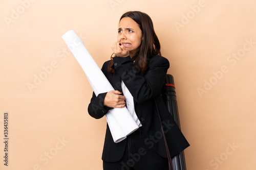 Young architect woman holding blueprints over isolated background is a little bit nervous