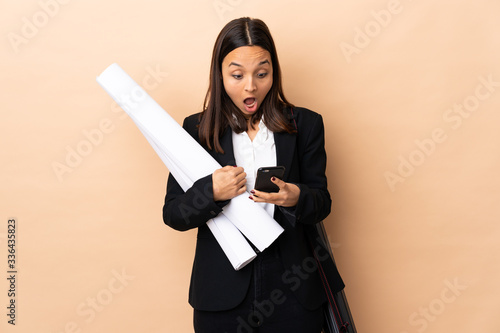 Young architect woman holding blueprints over isolated background surprised and sending a message