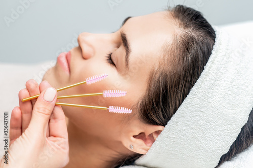 Eyelash brushes in hand on background of face of woman.