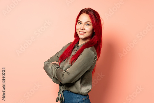Teenager red hair girl isolated on pink background with arms crossed and looking forward