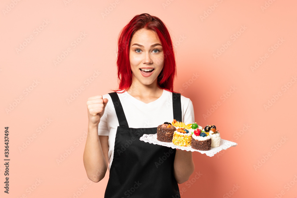 Pastry chef holding a muffins isolated on pink background celebrating a victory in winner position Pastry chef holding a muffins isolated on pink background celebrating a victory in winner position