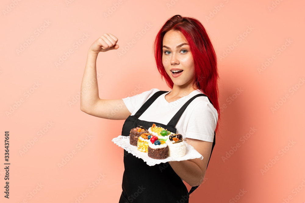 Pastry chef holding a muffins isolated on pink background doing strong gesture