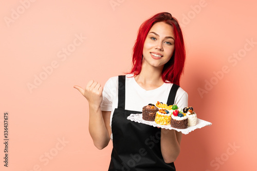 Pastry chef holding a muffins isolated on pink background pointing to the side to present a product