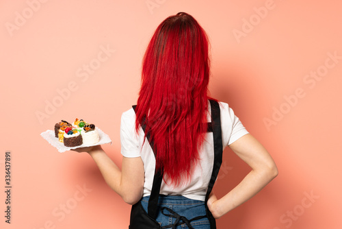 Pastry chef holding a muffins isolated on pink background in back position