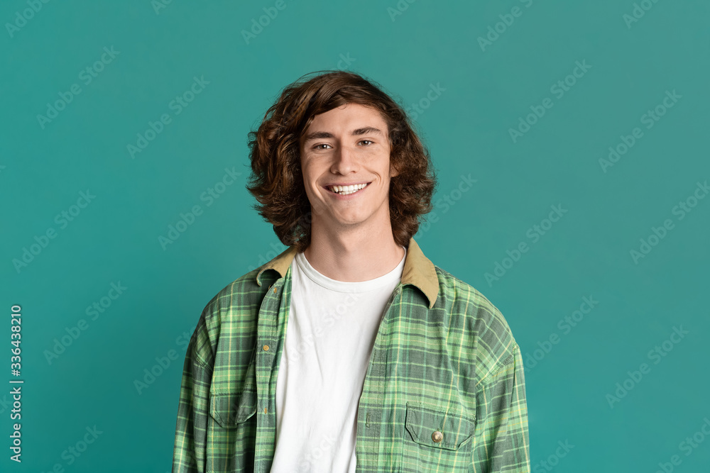 Cool millennial guy with curly hair smiling on turquoise backgrund Cool millennial guy with curly hair smiling on turquoise backgrund