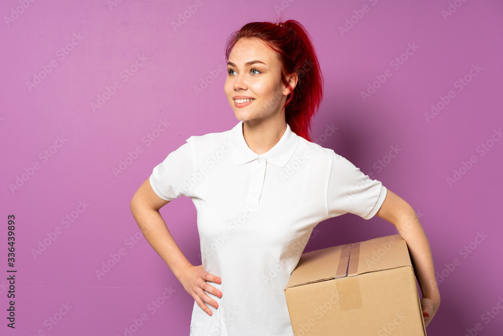 Teenager delivery girl isolated on purple background posing with arms at hip and smiling Teenager delivery girl isolated on purple background posing with arms at hip and smiling