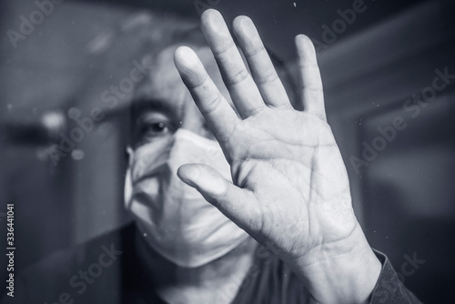 Portrait of man wearing a medical mask to protect against the corona virus confined behind a window