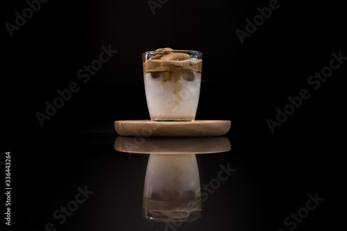 Iced Dalgona Coffee, a trendy korean style  cremy whipped coffee on fresh milk, and is reflection on black background
