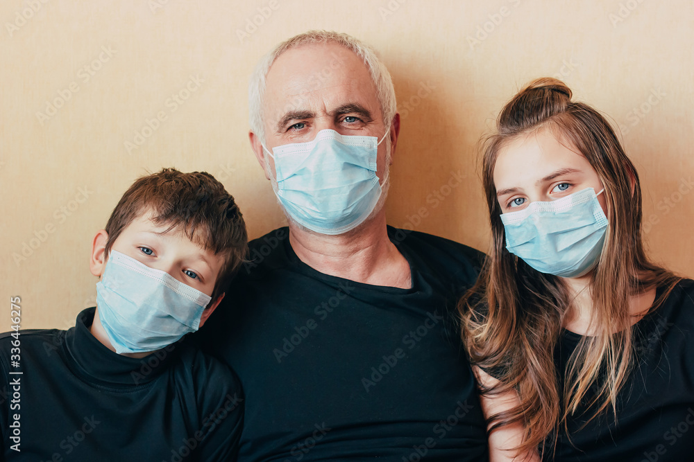 grandchildren  and grandfather in face masks look at camera and afraid of the consequences of the epidemic. Quarantined due to a sudden outbreak of coronavirus.Senior man with .kids on self isolation