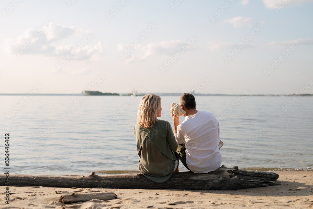 man and woman sit on the shore on a log and listen to the sink