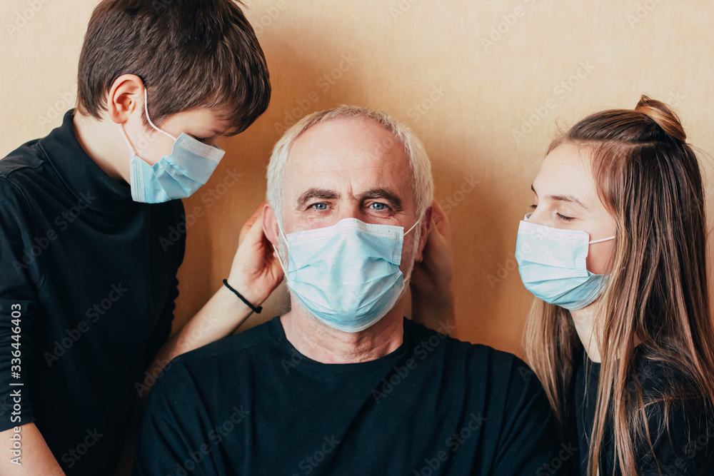 grandchildren put on a face mask on their grandfather and take care of him during quarantine and restrictions due to the outbreak of the coronavirus epidemic. children care about pensioner on pandemic