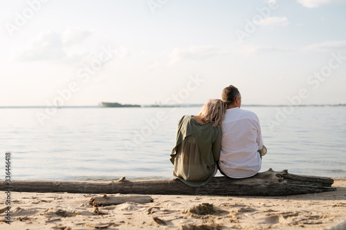 man and woman are sitting on a log by the sea and looking into the distance
