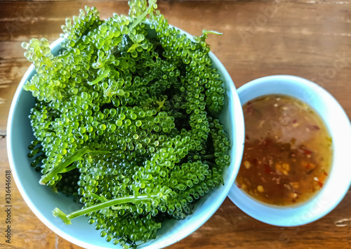 Bunch of seaweed, grapes in a blue cup and seafood sauce in a small white cup on the table.Bunch of seaweed or Sea Grapes.It is a high-fiber, low-calorie food. photo