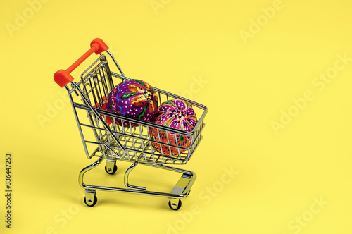 Beautiful bright hand-painted Easter eggs in a supermarket trolley on a yellow background