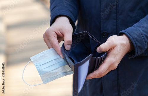 Man holds a medical mask and empty wallet without money. Bankruptcy and unemployment resulting from the global coronavirus epidemic.
