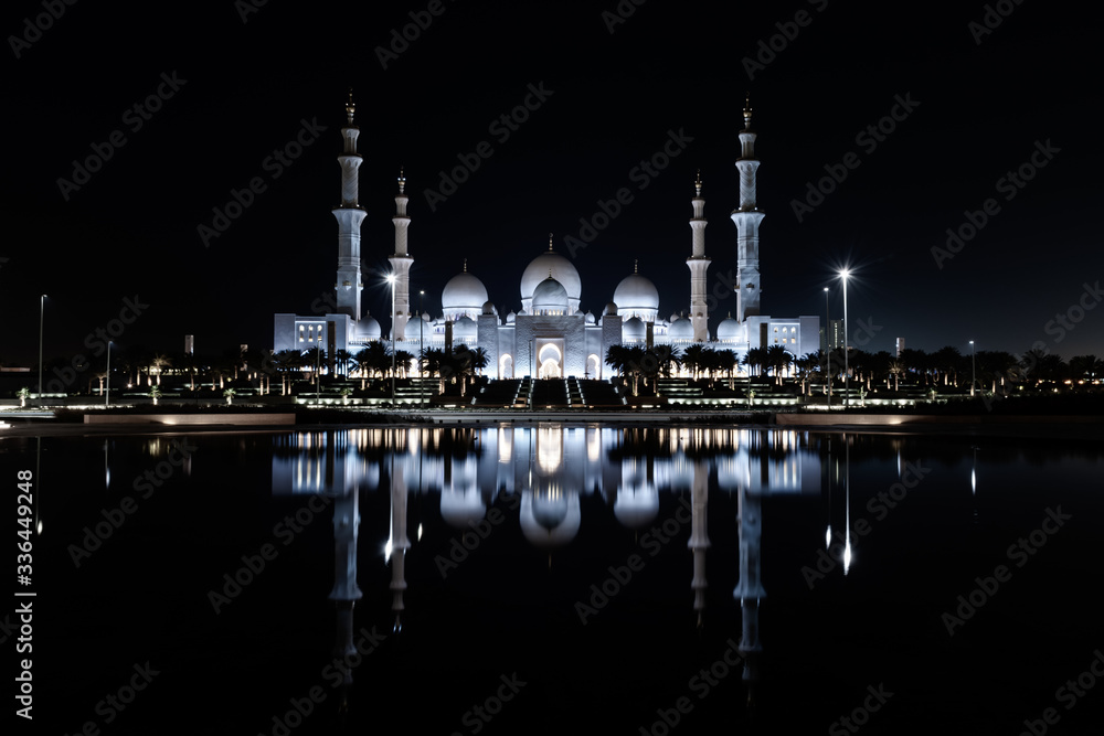 Iconic Islamic Site: Grand Mosque in Abu Dhabi, United Arab Emirates at night with a reflection in the pool showing off its beautiful colours of purple in the sky and water.