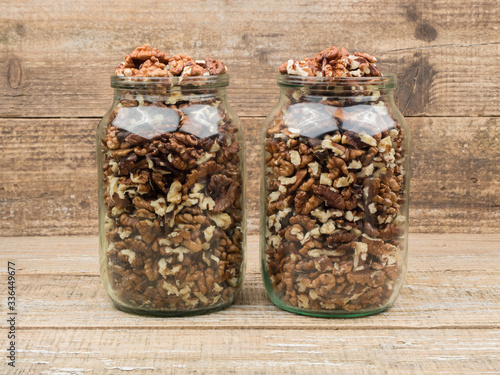 Walnut kernels in glass jars on wooden background.