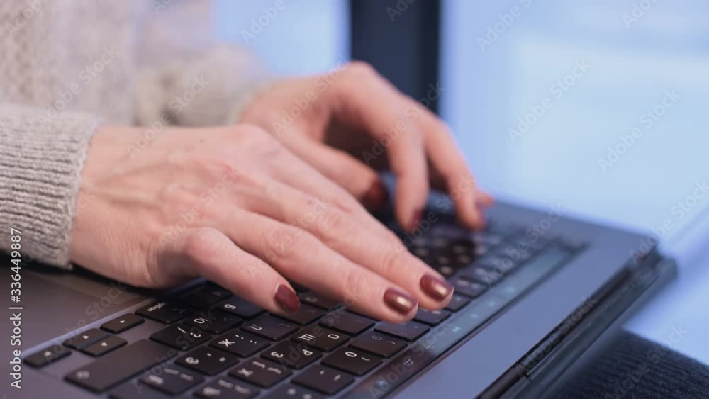 Close-up female hands typing on a laptop keyboard in the evening when the blue hour has already come outside the window. Shallow depth of field. winter forest in the background. Freelance concept Close-up female hands typing on a laptop keyboard in the evening when the blue hour has already come outside the window. Shallow depth of field. winter forest in the background. Freelance concept