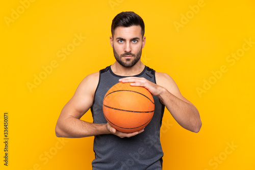 Man over isolated yellow background playing basketball