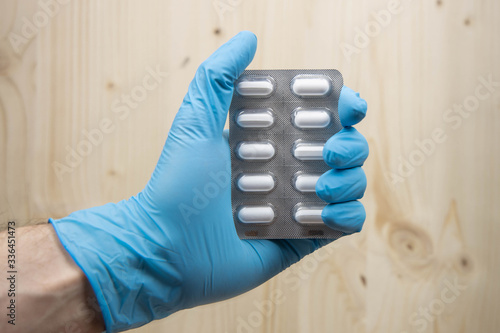 Hand with a glove holding a blister pack of medicine, selective focus