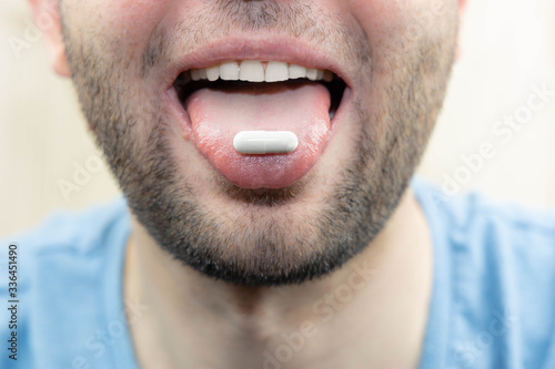 Young man with a pill on his tongue, selective focus